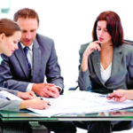 Four serious engineers looking at plans sitting at a table