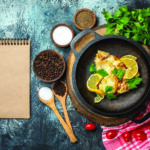 top view tasty fried fish with lemon and parsley in pan on wood